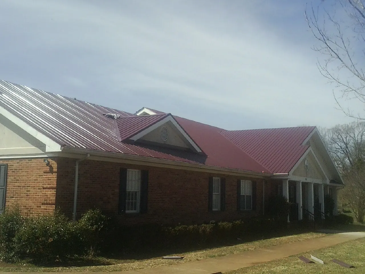 Red metal roof with gabled entries on a long brick building, from a Hail Damage Roof Repair job in Amador City