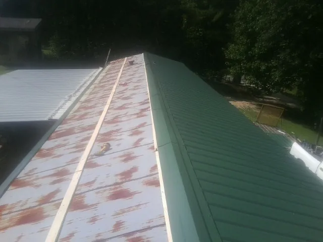 Old rusted panels beside newly installed green metal roofing — Wind Damage Roof Repair by Roofing Brothers in Amador City