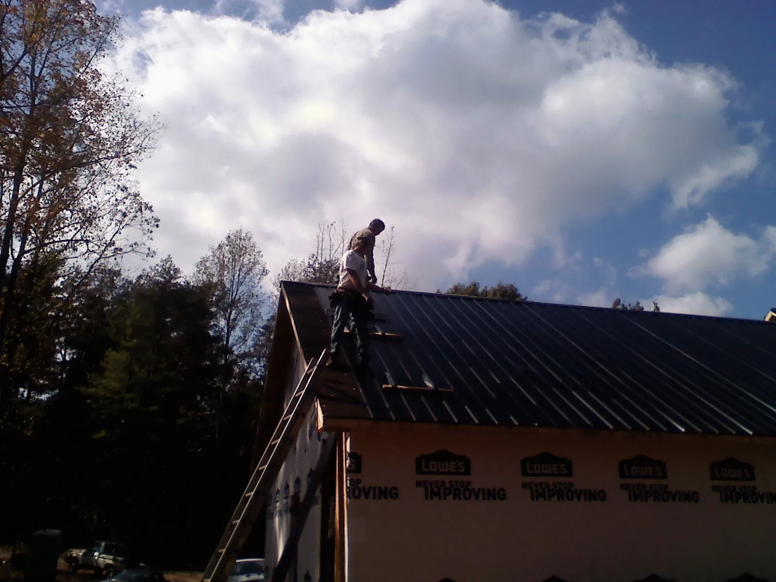Roofer fastening dark metal panels high against a cloudy sky, from a Roof Inspection job in Amador City