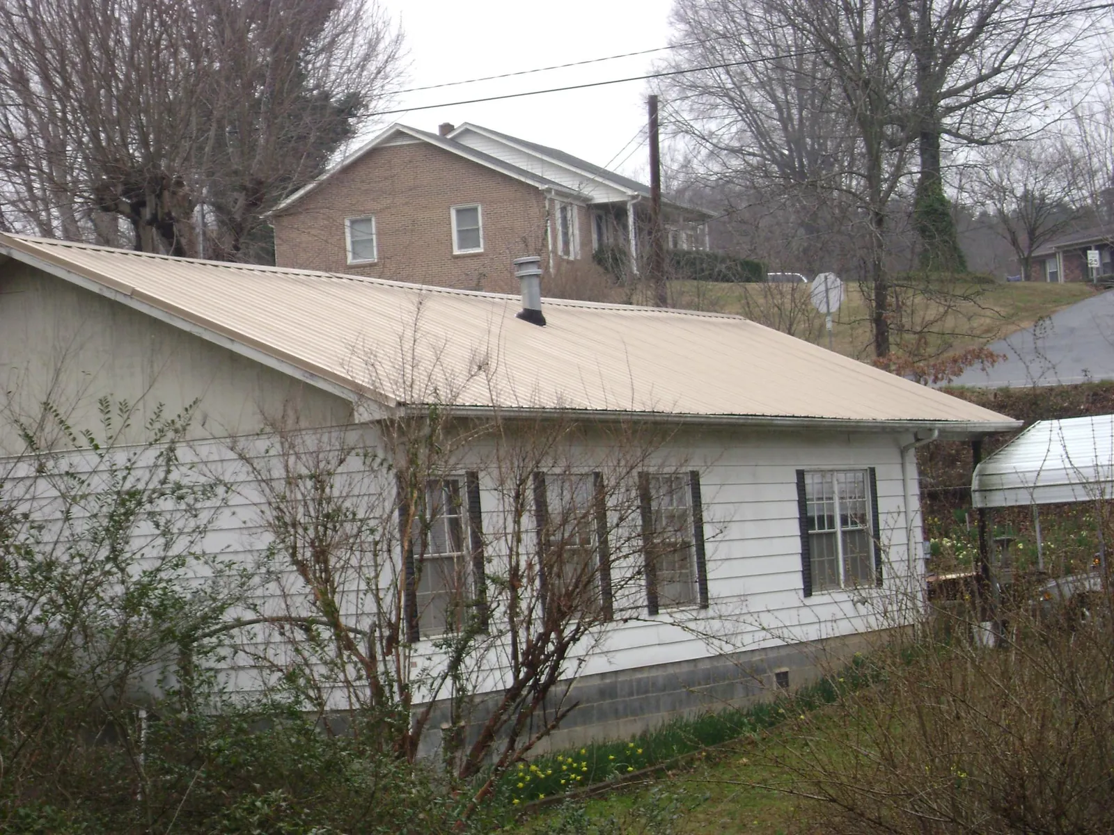 Tan metal roof on a white sided house set into a hillside — Commercial Roofing by Roofing Brothers in Amador City